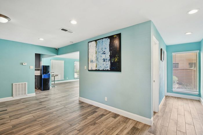 Bright and welcoming apartment interior with stylish wood flooring, modern teal walls, and vibrant artwork accentuating the open living space.