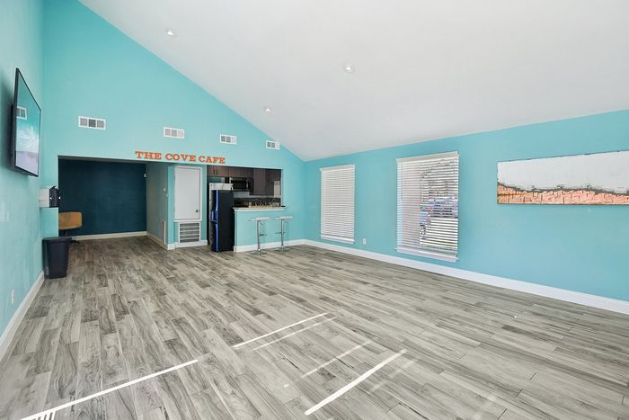 Inviting open space with teal walls, modern wooden flooring, and a cozy cafe nook. Bright natural light enhances the contemporary ambiance, perfect for relaxation or entertaining.