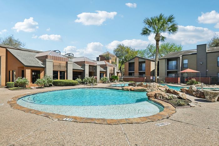 Charming apartment complex featuring a sparkling swimming pool and lush landscaping under a bright blue sky.
