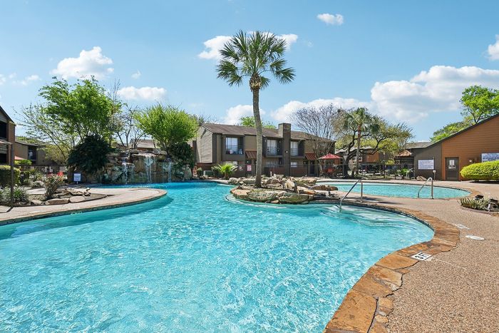 Luxurious apartment complex with a stunning outdoor pool, surrounded by lush greenery and a scenic waterfall feature, creating a serene oasis for residents.