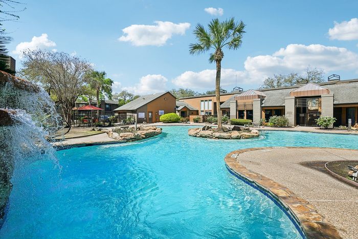 Luxurious apartment complex featuring a stunning outdoor pool with waterfall, surrounded by lush landscaping and modern architecture.