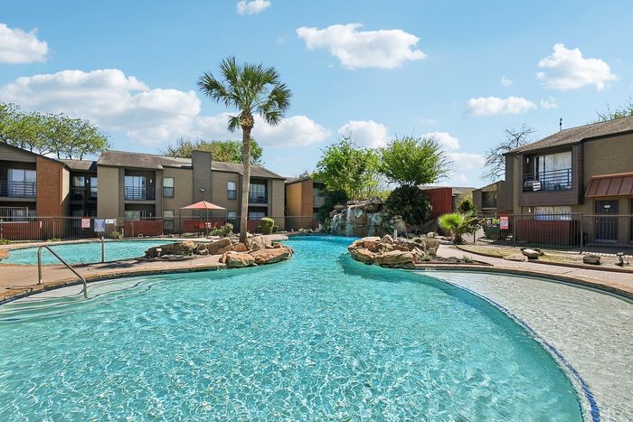 Inviting outdoor pool with waterfall feature surrounded by lush greenery and modern apartment buildings in a serene setting.