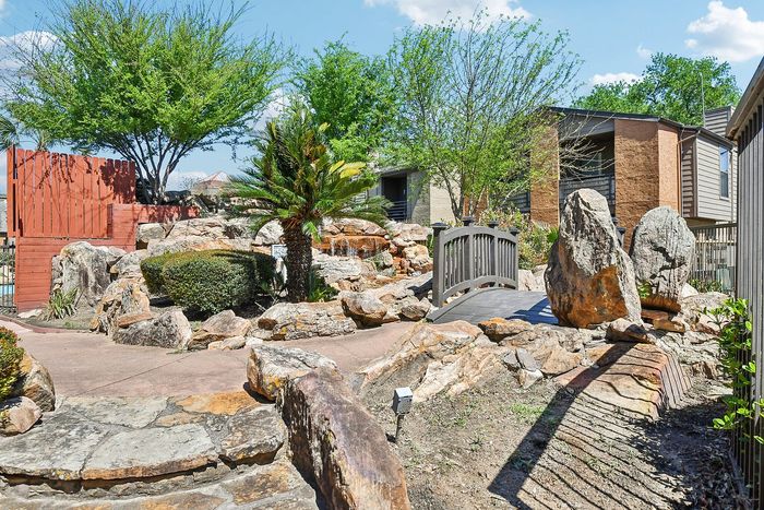 Serene garden oasis with stone pathways, lush greenery, and a charming bridge.