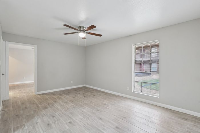 Bright and spacious room featuring elegant wood flooring, modern ceiling fan, and large window with blinds for ample natural light.