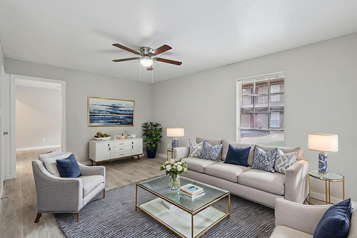 Elegant living room with modern decor, featuring a cozy white sofa, chic armchairs, and tasteful artwork, complemented by natural light through the window.