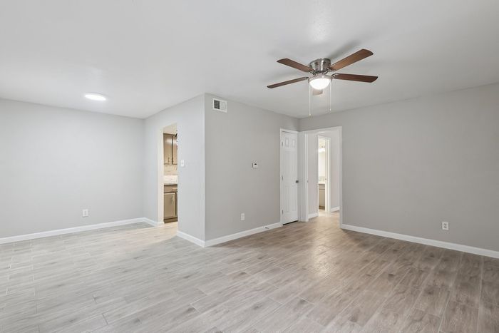 Bright and welcoming living space with wood-look flooring, modern ceiling fan, and seamless access to the kitchen and bathroom.