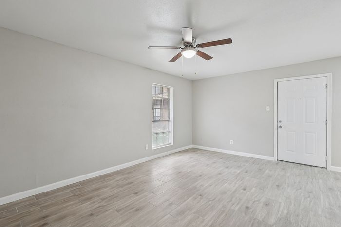 Bright and airy room featuring modern wood-look flooring, a sleek ceiling fan, and ample natural light from large windows. Perfect for a cozy living space.