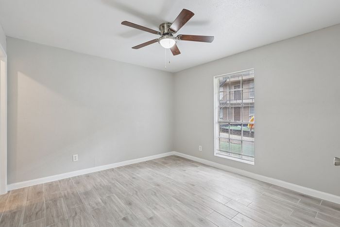 Bright and spacious room with elegant wood tile flooring and a modern ceiling fan, ideal for a cozy living space.