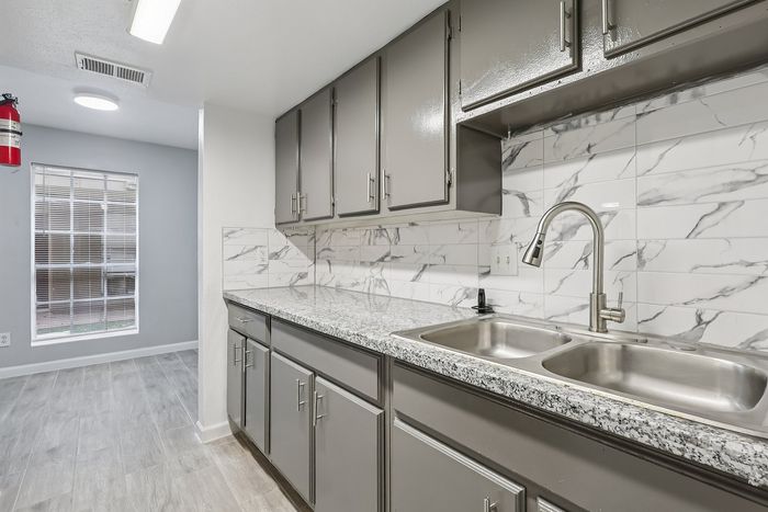 Chic kitchen featuring sleek gray cabinets, elegant marble backsplash, and stylish granite countertops.