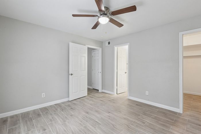 Bright and modern bedroom featuring sleek tile flooring, crisp white doors, and a stylish ceiling fan.