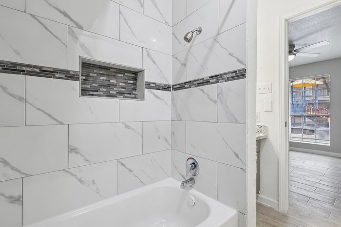 Elegant bathroom with marble-tiled walls and modern fixtures featuring a decorative mosaic design, with a glimpse of a bright and spacious room beyond.