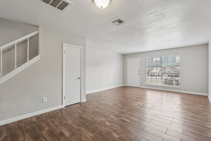 Bright and welcoming living room with sleek wooden flooring and ample natural light from large windows.