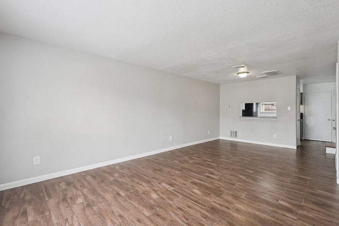 Spacious living area with elegant wood flooring and abundant natural light, featuring a pass-through window to the kitchen.