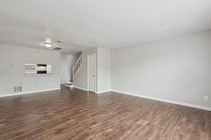 Elegant open-plan living space featuring sleek wooden flooring, modern finishes, and a cozy staircase leading to the upper floor.