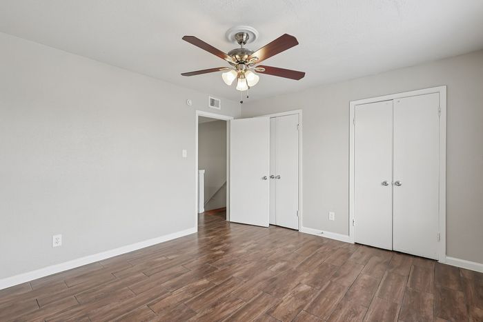 Bright bedroom with sleek wood flooring, ceiling fan, and ample closet space, offering a modern and inviting ambiance.