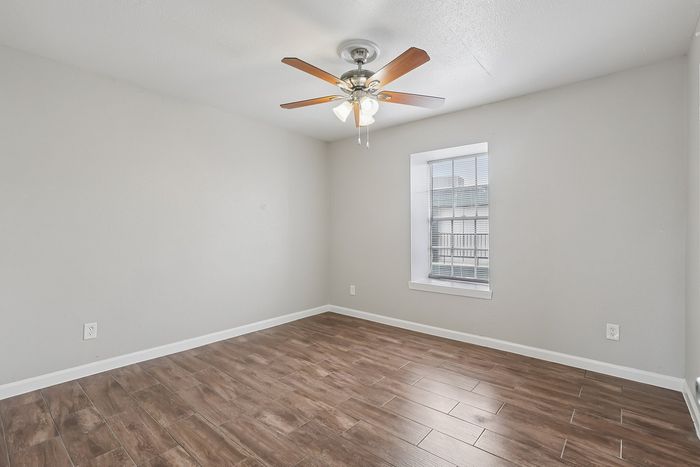 Bright and airy room with elegant wooden flooring and a stylish ceiling fan, perfect for a cozy retreat.