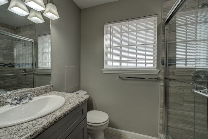 Modern bathroom with sleek granite countertop, elegant lighting, and a glass-enclosed shower with stylish tilework.
