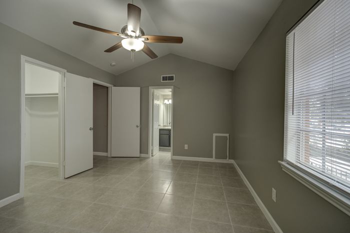 Inviting bedroom with a modern ceiling fan, spacious closet, and large window with blinds, offering natural light on elegant tile flooring.