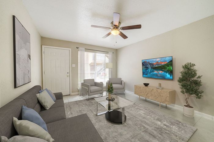 Modern living room with elegant gray sofas, stylish glass coffee table, and wall-mounted TV, complemented by natural light and chic decor.