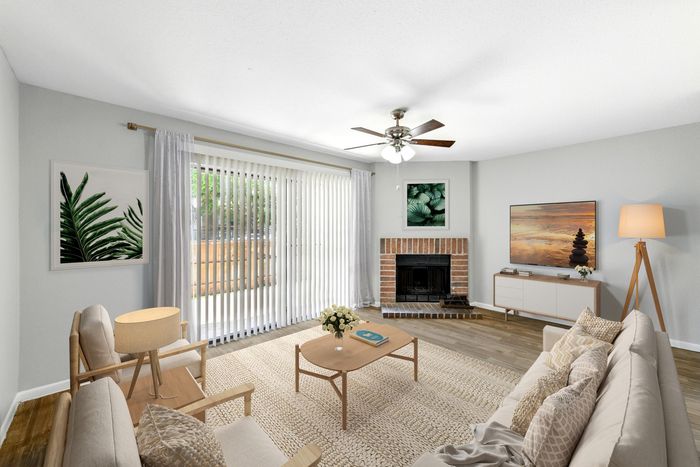Bright and modern living room featuring elegant wooden flooring, a cozy brick fireplace, and chic decor with natural light streaming through large vertical blinds.