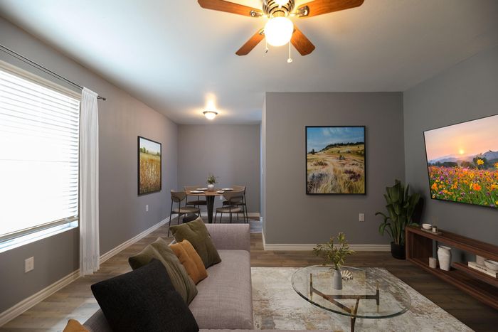 Elegant living room with modern decor, featuring a comfy sofa, glass coffee table, and vibrant artwork. Cozy dining area in the background offers a delightful atmosphere.