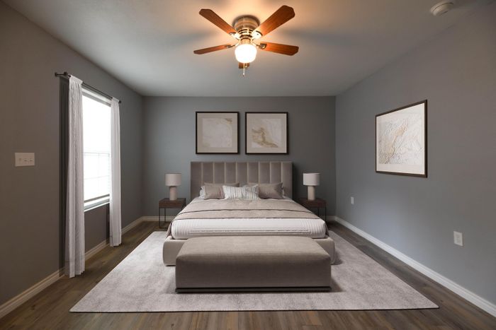 Elegant bedroom with plush bedding, soothing gray walls, modern ceiling fan, and natural light streaming through large window.