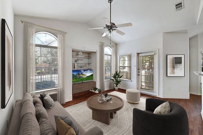 Bright and inviting living room with elegant decor, featuring a modern ceiling fan, cozy couch, sleek furniture, and abundant natural light from large windows.