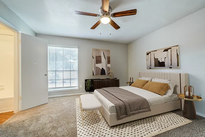 Inviting bedroom featuring a plush bed, modern ceiling fan, and elegant artwork, bathed in natural light.