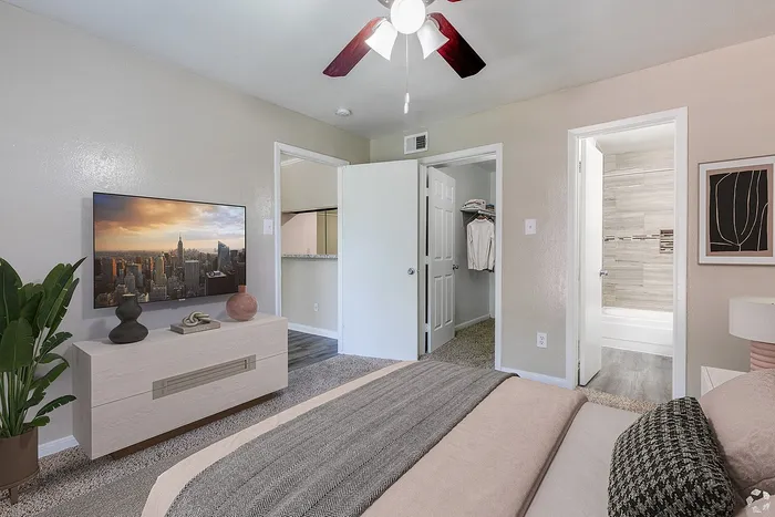 Chic apartment bedroom with cozy bedding, modern decor, and a flat-screen TV, featuring an ensuite bathroom and a walk-in closet.