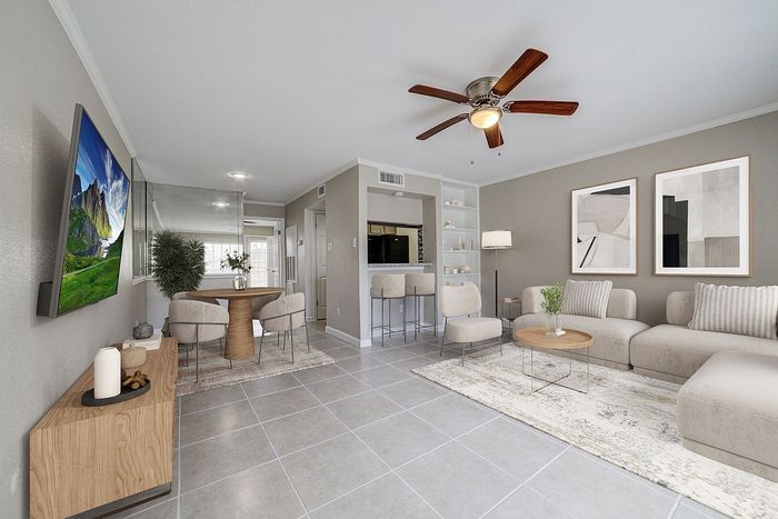 Modern and inviting living room with elegant decor, featuring a cozy beige sofa, stylish coffee table, bar seating by the kitchen, and a charming dining nook.