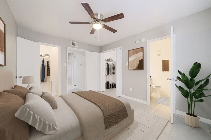 Inviting bedroom with cozy bedding, elegant ceiling fan, and spacious closets, enhanced by natural lighting and modern decor.