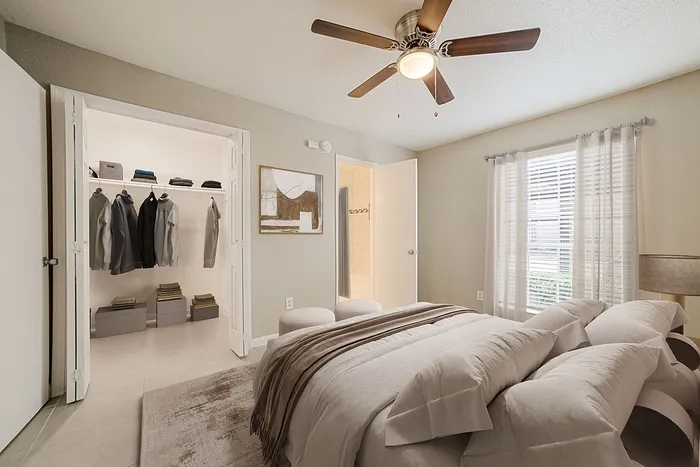 Inviting bedroom with plush bedding, modern ceiling fan, and adjacent walk-in closet featuring ample storage space.
