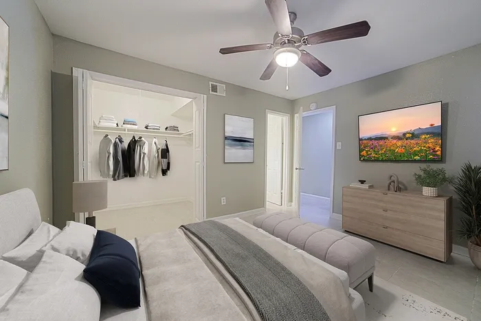 Inviting bedroom with modern ceiling fan, cozy bed, stylish decor, spacious walk-in closet, and scenic wall art.