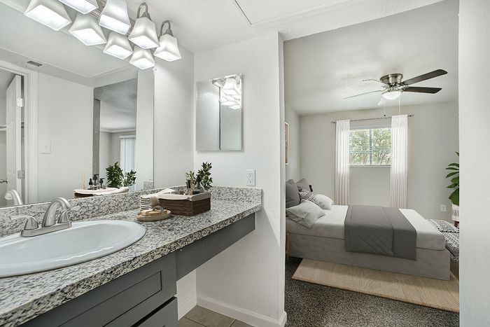 Modern bathroom with granite countertop and elegant lighting, leading to a cozy bedroom with natural light and stylish decor.