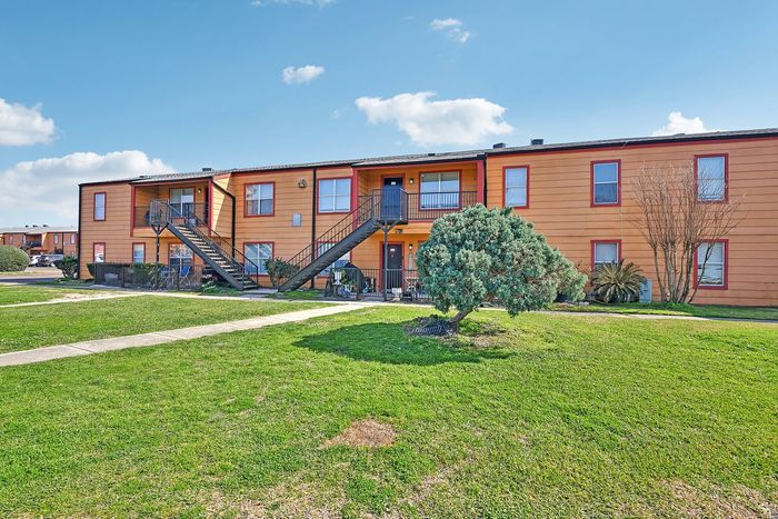 Charming apartment complex with vibrant orange facade, surrounded by lush green lawns and clear blue skies, offering a welcoming and tranquil atmosphere.