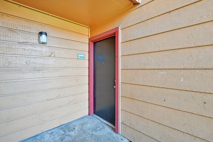 Charming apartment entrance with a modern black door and vibrant red trim, set in a warm wood-paneled exterior with a welcoming atmosphere.