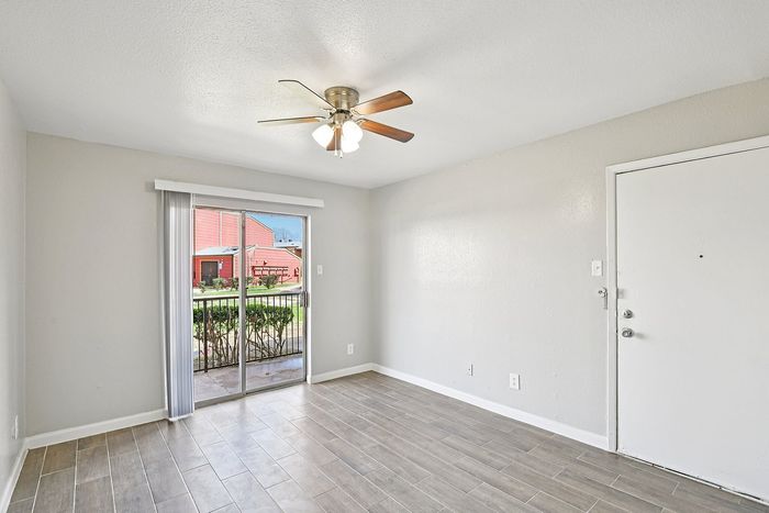 Bright living area with sleek wooden flooring, ceiling fan, and large sliding glass door leading to a sunny outdoor space.