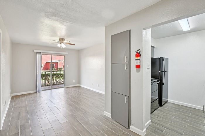 Bright open living area with modern tile flooring and sliding glass doors leading to a lush outdoor view, adjacent to a sleek kitchen with contemporary appliances.