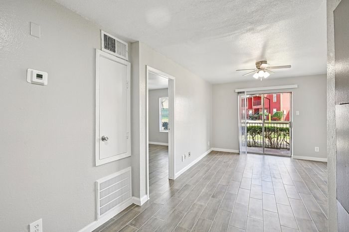 Bright and inviting open-space living area with modern wood flooring, ceiling fan, and sliding glass door leading to a charming outdoor view.