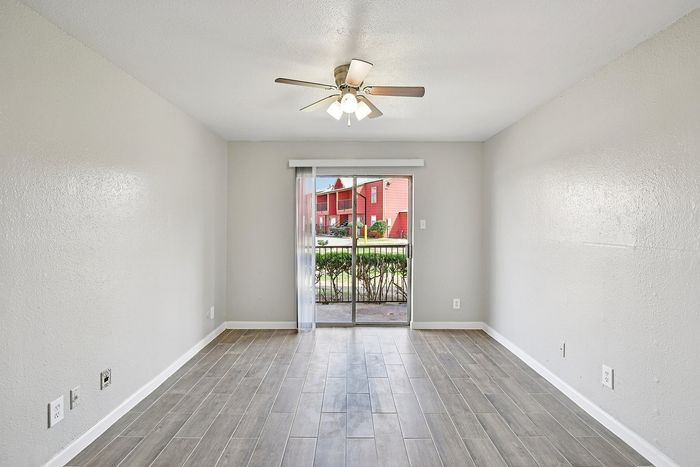 Bright living space with elegant wood-look flooring, ceiling fan, and sliding glass doors leading to a charming outdoor view.