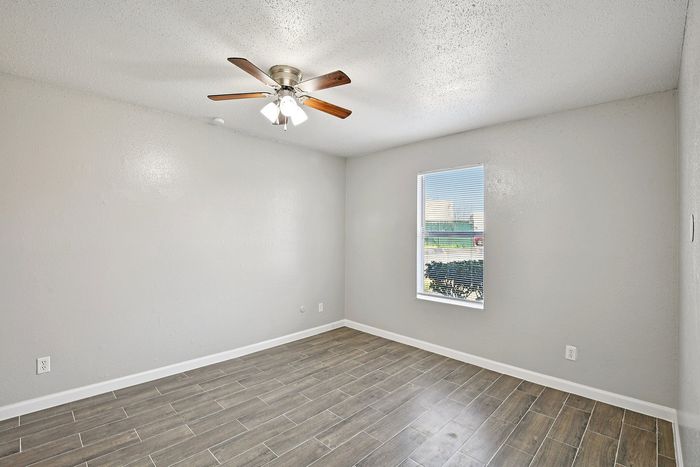 Bright, spacious room with sleek wooden flooring and a modern ceiling fan, featuring a large window for natural light.
