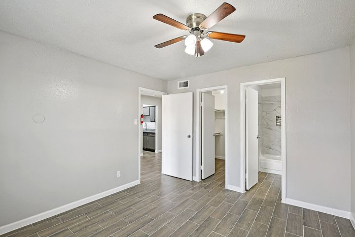 Bright, modern bedroom with tiled flooring, ceiling fan, and convenient access to a stylish bathroom and a cozy kitchen.