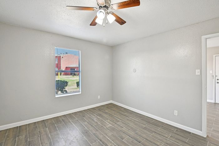 Bright, cozy room with a stylish wooden floor, modern ceiling fan, and a large window offering natural light and a pleasant view.