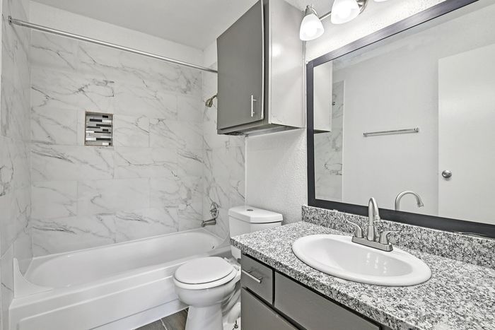 Modern bathroom with elegant marble tile walls, sophisticated vanity with granite countertop, and bright overhead lighting.