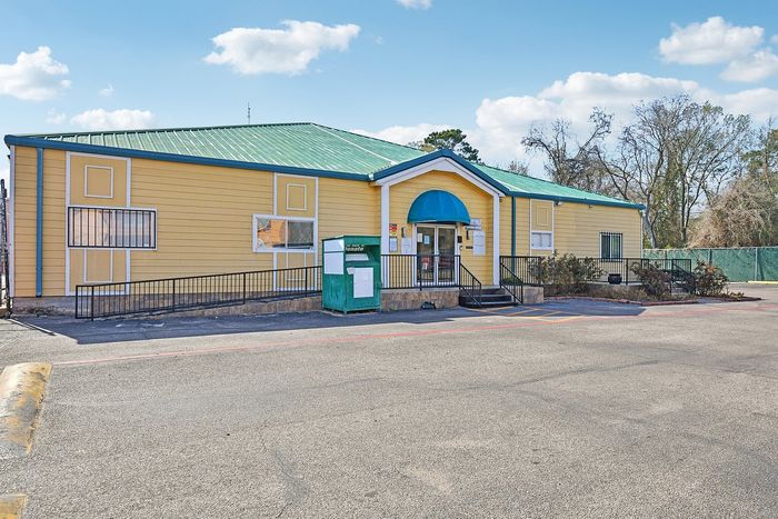 Charming yellow building with green roof and welcoming entrance, set against a vibrant sky backdrop.