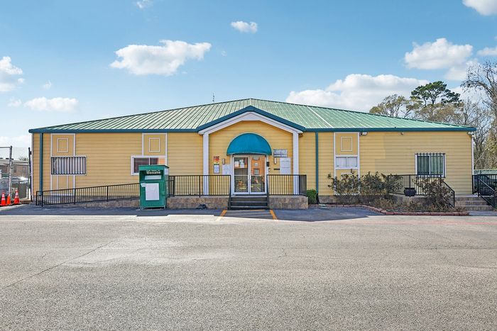 Charming yellow building with green roof featuring a welcoming entrance, perfect for a community space with ample parking.