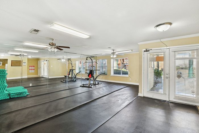 Spacious fitness room with mirrored walls, exercise equipment, and ample natural light.