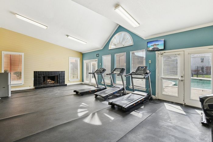 Inviting fitness room with modern treadmills, abundant natural light, cozy fireplace, and poolside views.