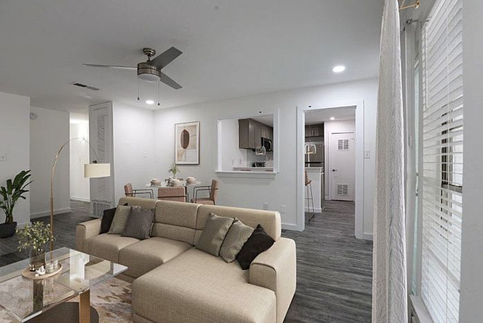 Modern living room with elegant decor, featuring a cozy beige sofa, chic coffee table, and an open layout leading to a sleek kitchen and dining area.