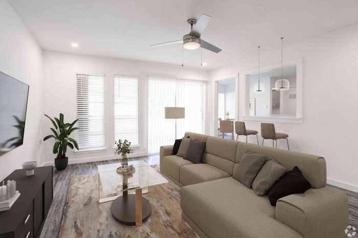 Modern living room with cozy sectional, sleek ceiling fan, and elegant glass coffee table bathed in natural light.